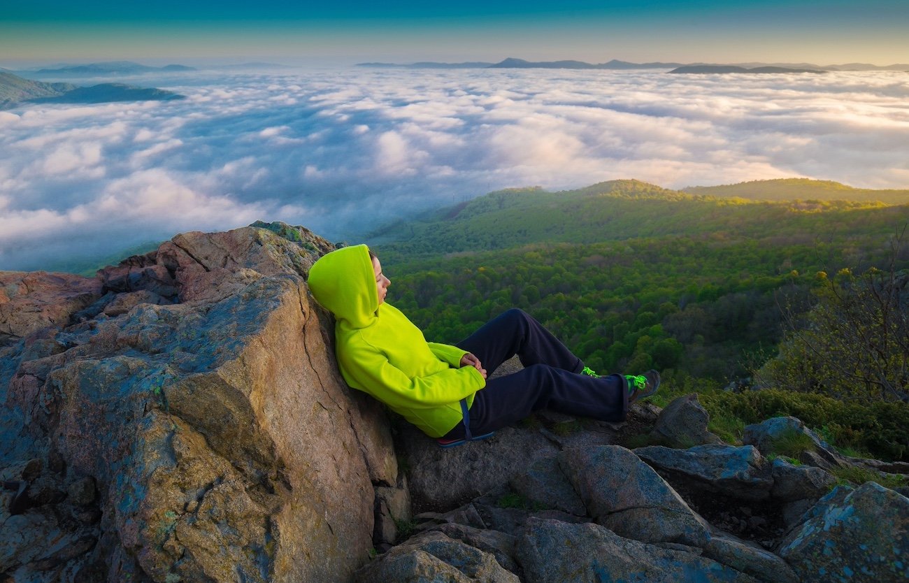 Woman sitting on a rock above clouds.