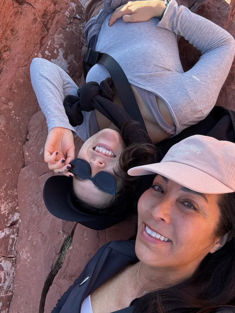 Two women resting on smooth red rocks overlooking the canyon landscape in Sedona.
