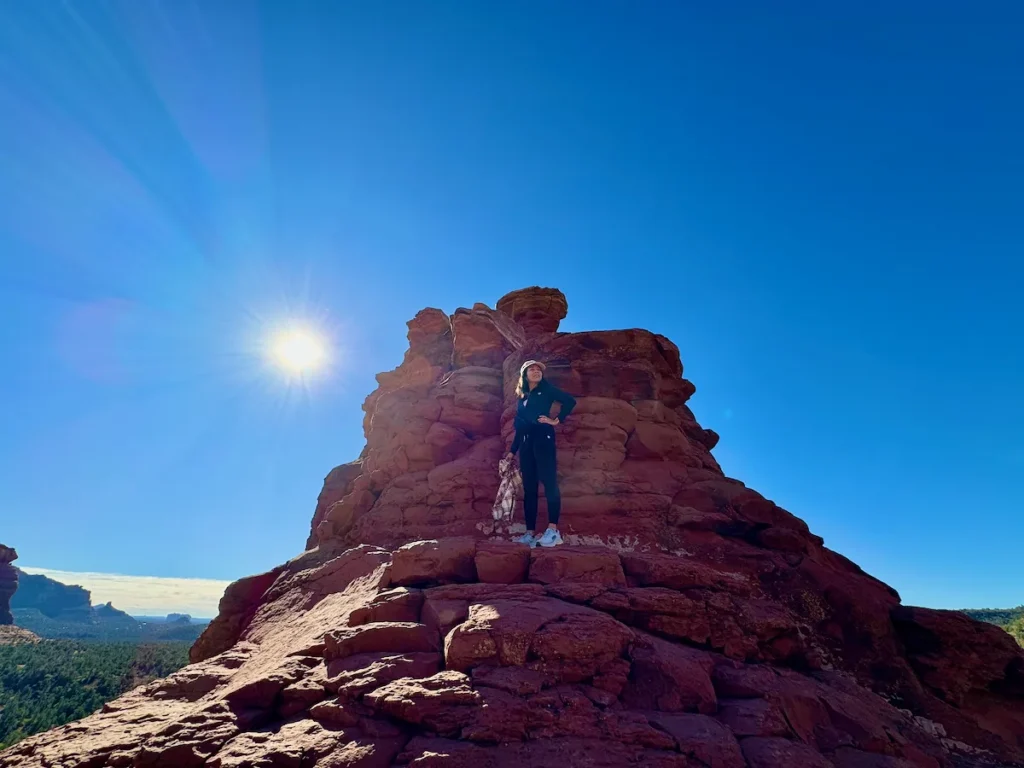 Hiker standing on a red rock formation with sunburst over Boynton Canyon in Sedona.