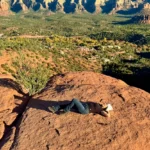 Phoebe relaxing on a red rock overlook with panoramic Sedona canyon and mesa views.