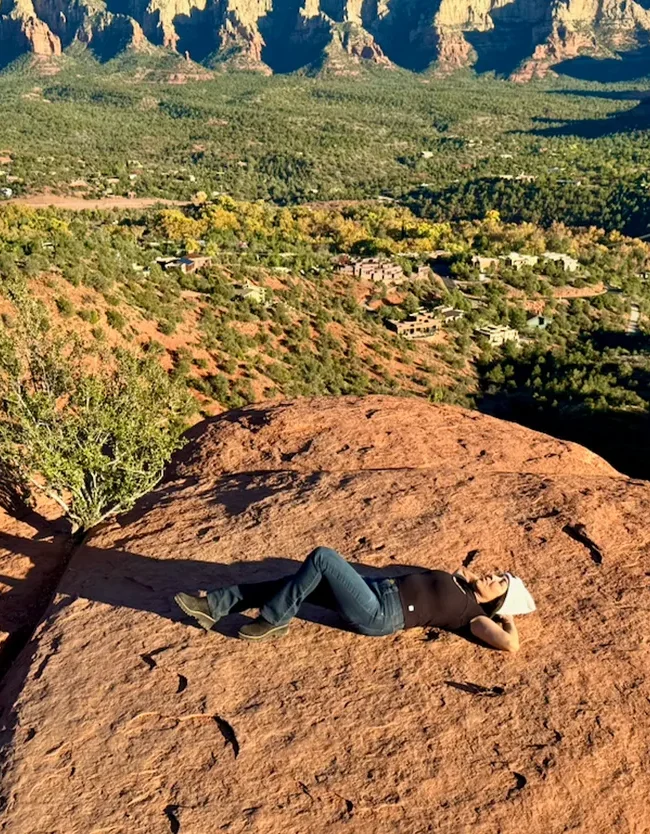 Phoebe relaxing on a red rock overlook with panoramic Sedona canyon and mesa views.