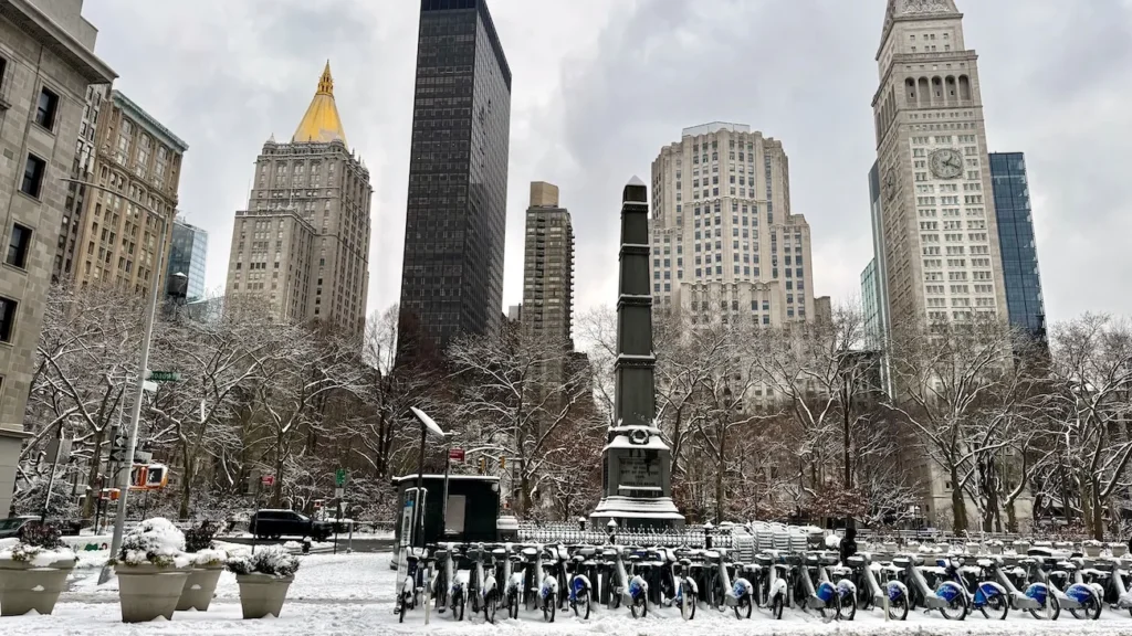 Snow-covered Madison Square Park with monument and Flatiron District skyline in New York City