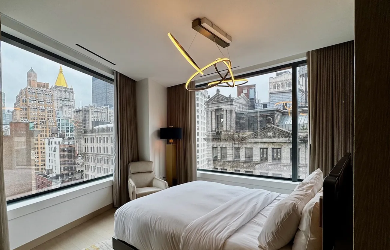 Luxury hotel bedroom with floor-to-ceiling windows overlooking historic New York City buildings at The Ritz-Carlton NoMad