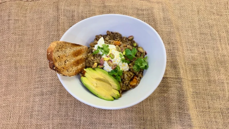 Bowl of savory lentil quinoa soup topped with Greek yogurt, avocado, pistachios, cilantro, and served with toasted multigrain bread.
