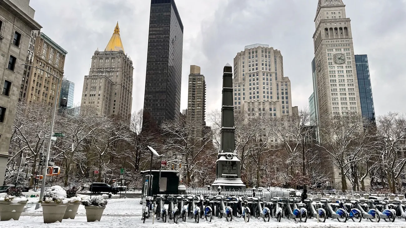 Snow-covered Madison Square Park with monument and Flatiron District skyline in New York City