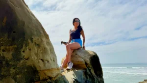 Phoebe Chongchua sitting on coastal rocks reflecting on strength, wellness, and healthy aging in midlife