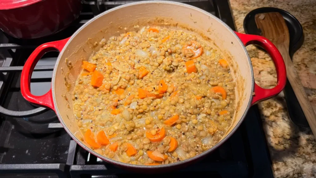 Homemade savory lentil quinoa soup simmering in a Dutch oven with green lentils, carrots, onions, and quinoa.